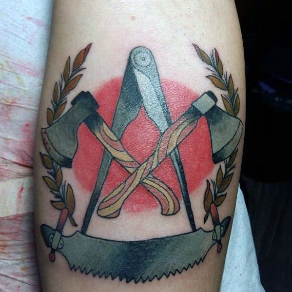 Colorful tattoo featuring crossed axes, a compass, and a saw with a red background and laurel branches, symbolizing craftsmanship and strength.