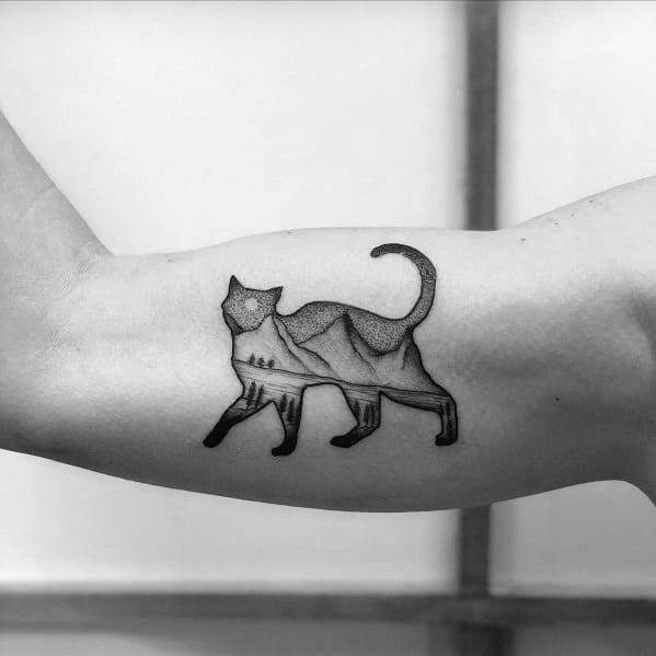 Minimalist cat tattoo with a mountain landscape inside its body, blending nature and feline grace in a creative design.