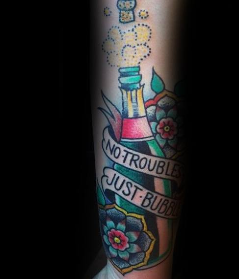 Colorful tattoo of a champagne bottle with flowers and a banner that reads “No troubles, just bubbles,” surrounded by fizz and sparkles.