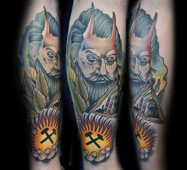Colorful tattoo of a horned figure holding a glowing orb with crossed pickaxes, surrounded by flames, leaves, and mining buildings.