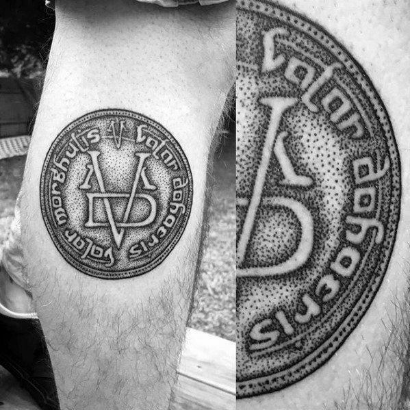 Detailed tattoo of a Valar Morghulis coin from Game of Thrones, featuring dotwork shading and intricate lettering for a bold design.