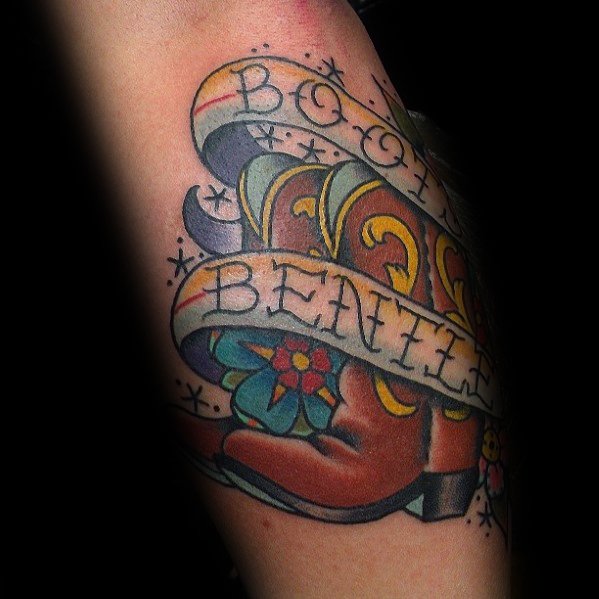 Tattoo of a cowboy boot wrapped in a banner reading "Boots & Beauties," featuring floral details and bold Western-inspired design elements.