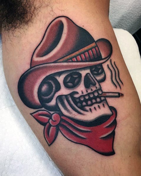 Tattoo of a cowboy skull with star-shaped eyes, wearing a brown hat and red bandana, smoking a cigarette, done in bold traditional style.