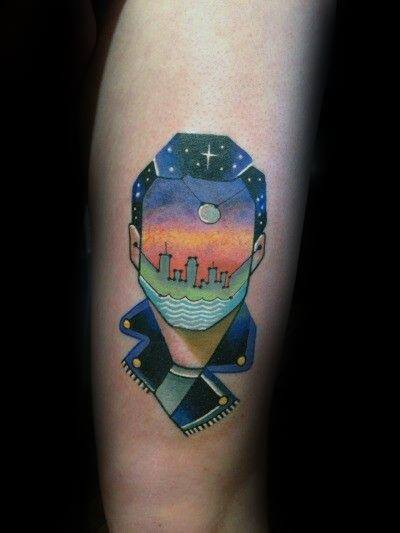 Surreal tattoo of a faceless figure with a sunset cityscape inside, blending geometric shapes, cosmic elements, and vibrant colors.