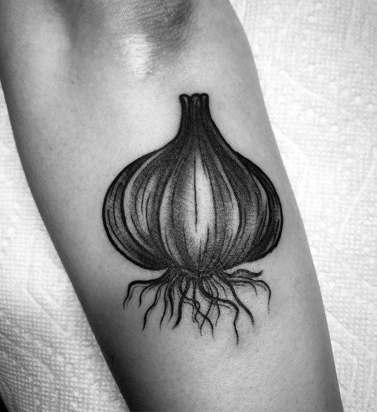 Black and grey garlic tattoo with fine shading and detailed roots, creating a bold and realistic botanical design on the arm.