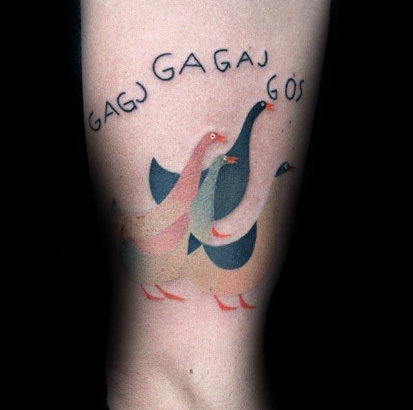 Whimsical tattoo of three stylized geese in soft pastel colors, with the playful text "GAGJ GAGAJ GÖS" above them, inked on the forearm.