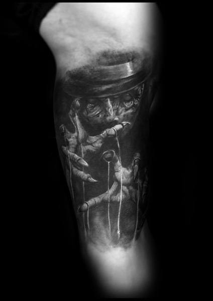 Black and grey tattoo featuring a sinister puppet master in a top hat, controlling marionette strings with eerie, detailed shading for a gothic look.