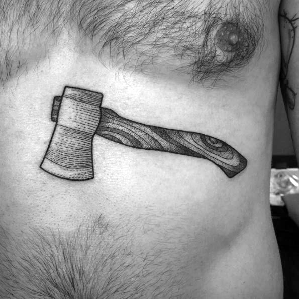 Black and grey hatchet tattoo on the ribcage with detailed wood grain texture on the handle and fine dotwork shading on the blade.