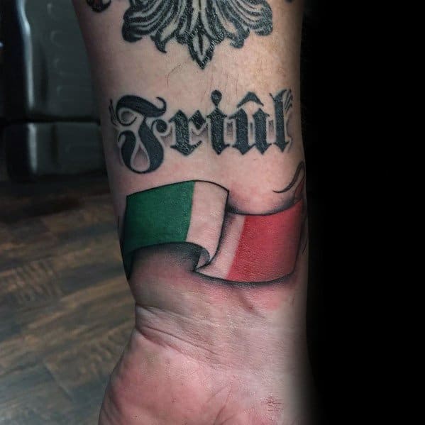 Wrist tattoo featuring a waving Italian flag ribbon with the word "Friûl" above it, representing regional pride and cultural heritage.