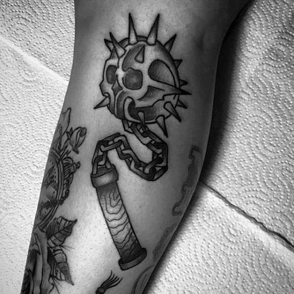 Black and gray mace tattoo featuring a spiked ball with a skull design, connected by a chain to a textured handle, symbolizing power and mortality.