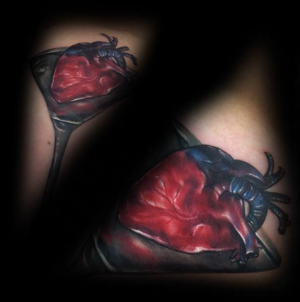 Realistic martini glass tattoo featuring an anatomical heart as the drink. A bold and dramatic design with rich shading and deep red tones.