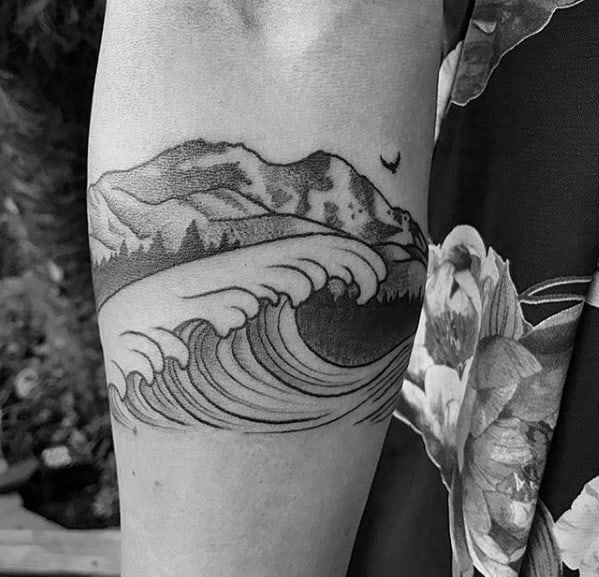 Black ink tattoo featuring a bold wave crashing beneath a mountain range, combining fine linework and shading for a balanced nature-inspired design.