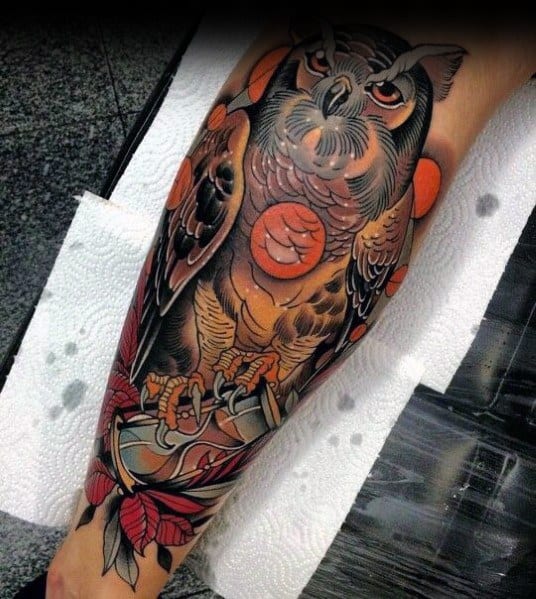 Neo-traditional owl tattoo with bold shading, orange moon accents, and intricate details, featuring sharp talons gripping a dagger.