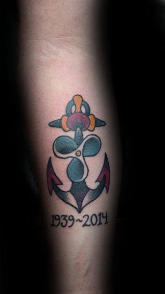 Traditional-style memorial tattoo on the forearm featuring an anchor and propeller design with bold colors and the years "1939-2014" underneath.