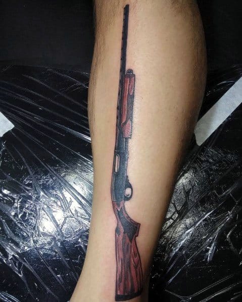 Detailed shotgun tattoo on the leg featuring a sleek black barrel and red-toned wooden stock, designed with bold shading and fine linework.