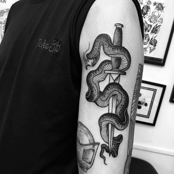 Black and grey snake and dagger tattoo on upper arm, featuring bold lines, intricate shading, and a classic traditional design.