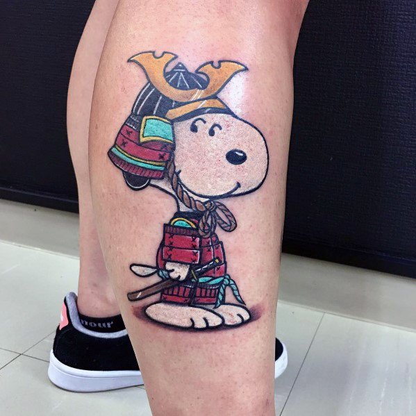 Colorful tattoo of Snoopy dressed as a samurai, wearing detailed armor and a golden helmet, holding a small sword on a person's leg.