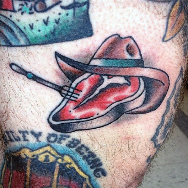 Tattoo of a steak wearing a cowboy hat, pierced by a fork, blending Western and food themes with bold outlines and shading for a fun design