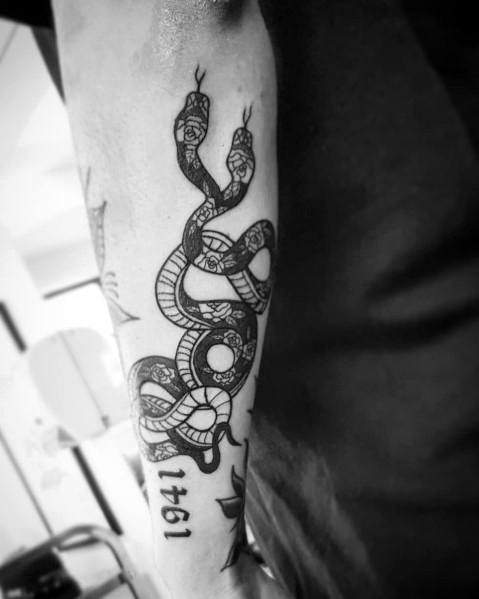Black and grey two-headed snake tattoo on the forearm, featuring intricate patterns and bold lines for a striking and symbolic design.