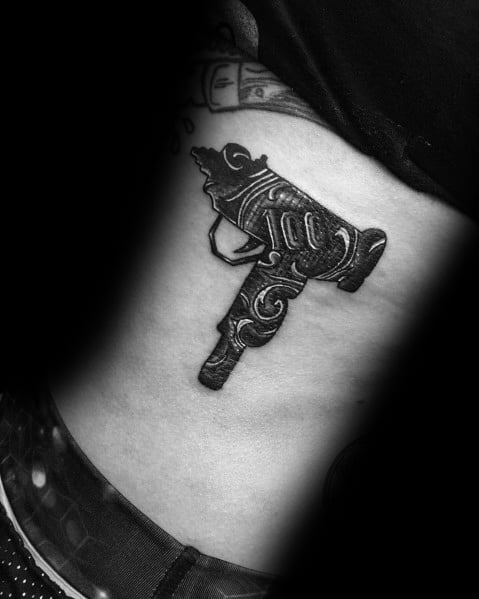 Black and grey Uzi tattoo on the side torso with intricate ornamental engravings, blending firearm and decorative art styles.