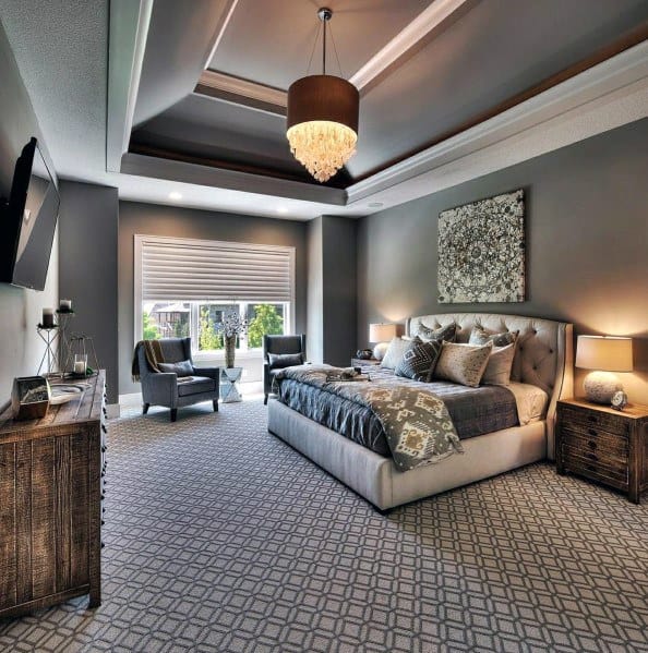Modern bedroom with patterned carpet, tufted bed, elegant chandelier, and cozy seating area.