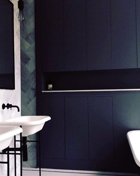 Navy blue bathroom cabinets with white sinks and chevron tile accent wall.