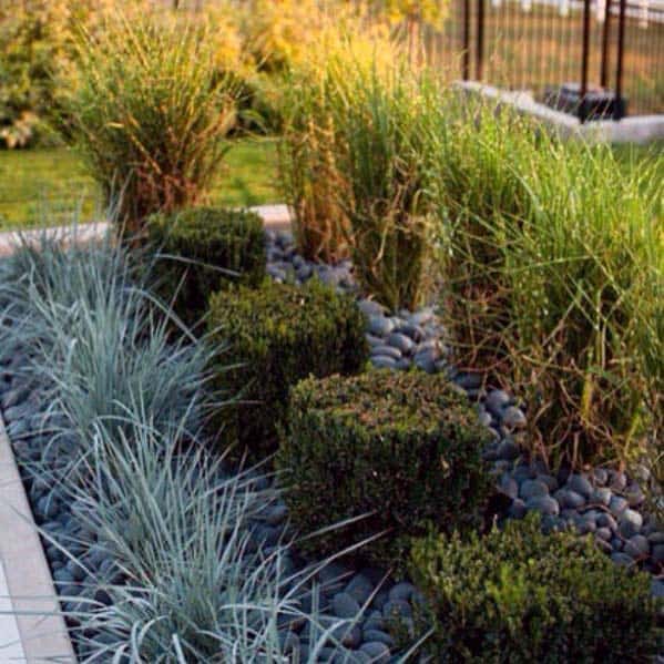Impressive river rock landscaping with neatly trimmed boxwoods and ornamental grasses, adding texture and structure to the garden bed.