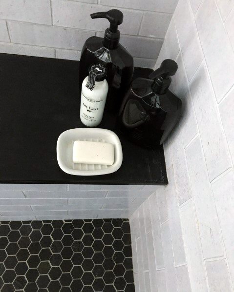 Shower corner with black hexagon tiles, soap dish, and black bottles on a sleek black ledge.