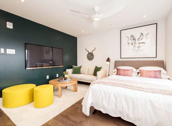 Bright studio with green accent wall, cozy bed, modern sofa, and vibrant yellow stools.