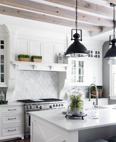 White kitchen with black pendant lights, exposed beams, and a clean white island.