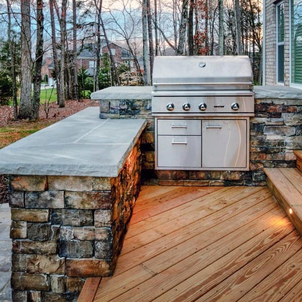 Outdoor stone patio with a built-in grill, surrounded by trees