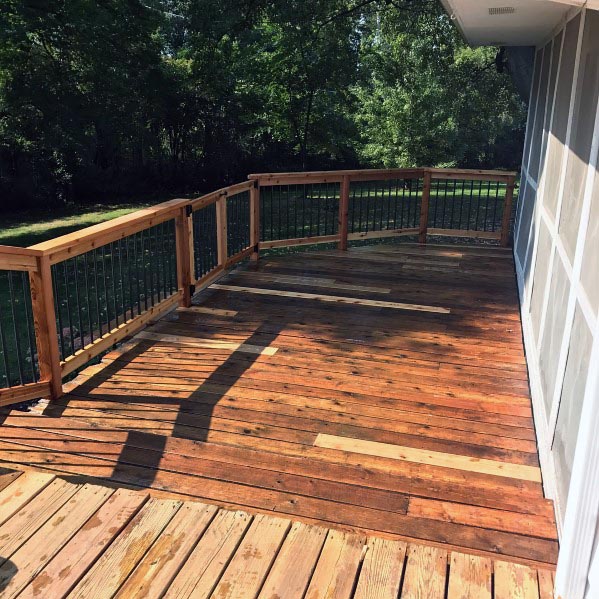 Sunny wooden deck with railing and a gate, surrounded by trees