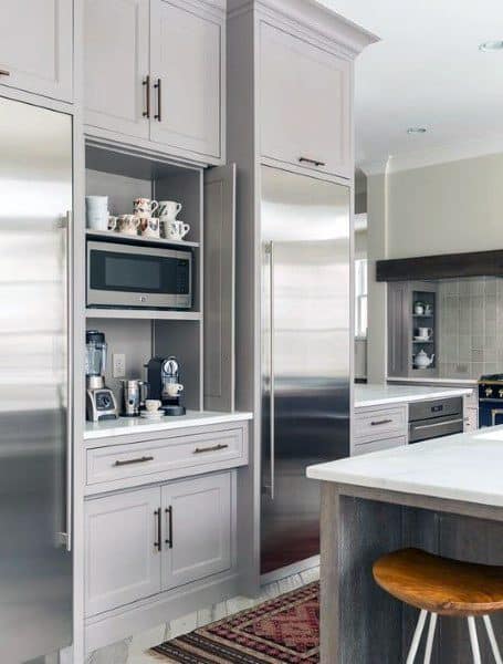 Built-in coffee bar with grey cabinets, microwave, coffee machines, and open shelving.