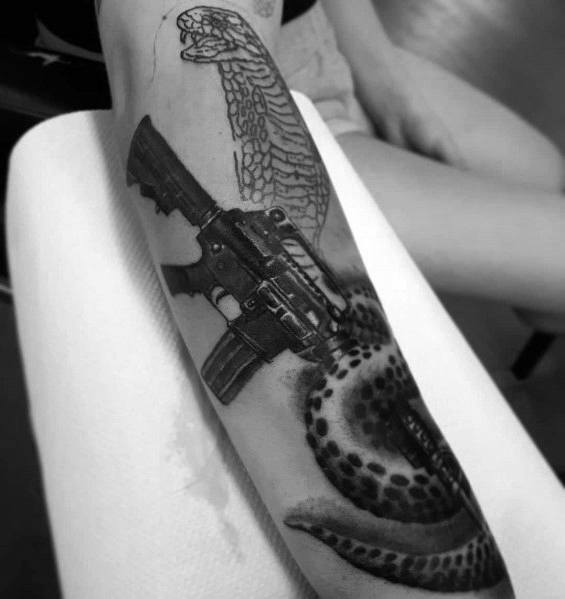 Black and grey tattoo featuring an AR-15 entwined with a cobra, symbolizing power, danger, and resilience with detailed shading and depth.