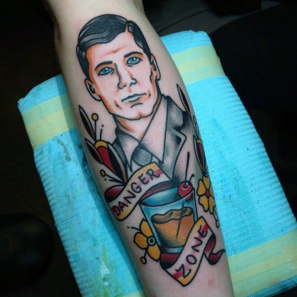 Traditional-style Archer tattoo featuring the spy in a suit, a 'Danger Zone' banner, vibrant floral details, and a whiskey glass.
