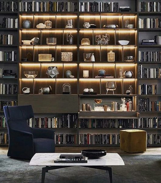 Modern living room with a backlit display bookcase, armchair, and sleek coffee table.