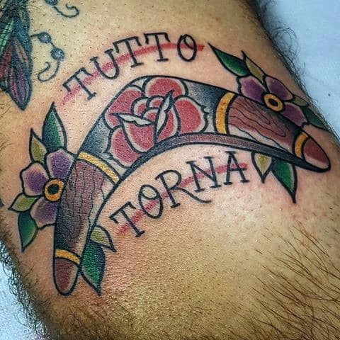 Traditional-style boomerang tattoo with flowers and the phrase TUTTO TORNA in bold script, symbolizing the return of all things.