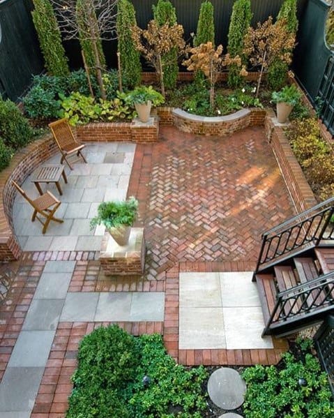 Aerial view of a garden patio with brick paving, lush plants, and wooden chairs