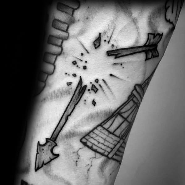 Black and grey broken arrow tattoo with an explosion effect at the snap point and a broad, jagged arrowhead on the forearm.