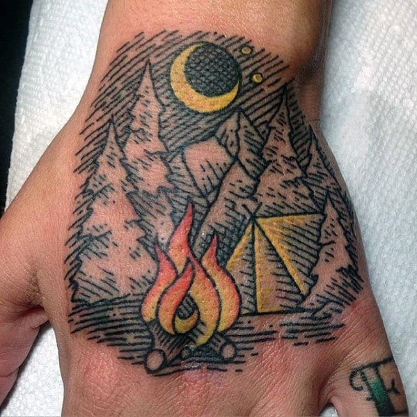 Hand tattoo of a campfire, tent, trees, and mountains under a crescent moon, done in a bold linework and stippling style.