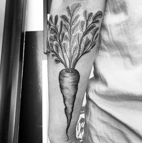Intricate black ink carrot tattoo on the forearm with fine line detailing, realistic shading, and lush leafy tops for a bold botanical design.