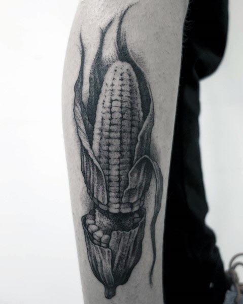 Black and gray tattoo of a realistic corn cob with husks, featuring fine shading and intricate details for a bold and classic design.