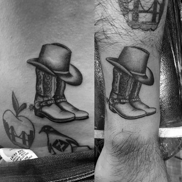 Black and gray tattoo of a detailed cowboy hat resting on a pair of ornate cowboy boots, done in a realistic Western style with fine shading.