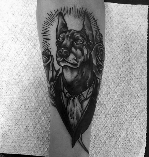 Black and grey Doberman tattoo with a formal suit, halo rays, and roses, blending elegance, strength, and symbolism in a bold design.