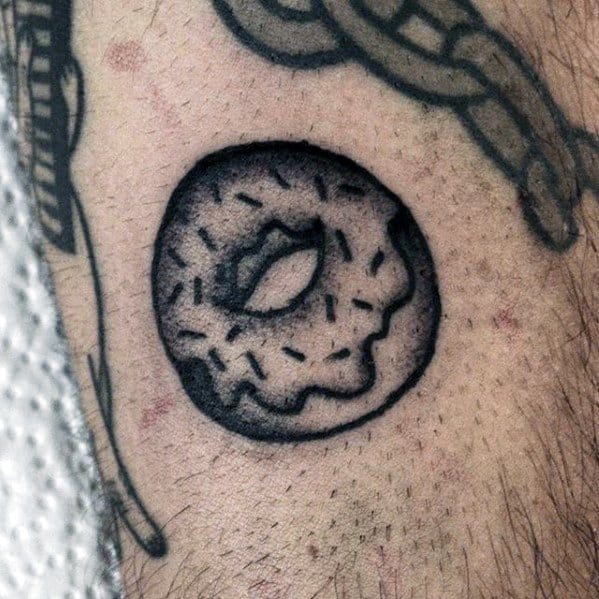 Black and grey tattoo of a donut with sprinkles, shaded for a bold, minimal look with a classic old-school style.
