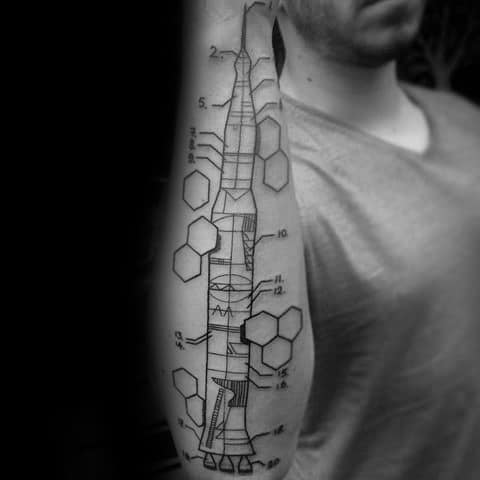 Tattoo of a technical diagram of a rocket with numbered labels and hexagonal elements, combining science, engineering, and art on the forearm.