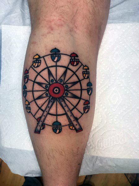 Traditional-style Ferris wheel tattoo with bold black outlines, vibrant red, yellow, and blue gondolas, and a classic symmetrical design on the leg.
