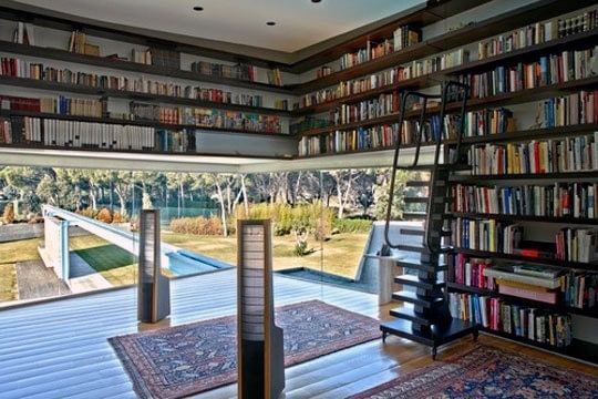 Modern library room with large window, bookshelf ladder, and view of a lush garden