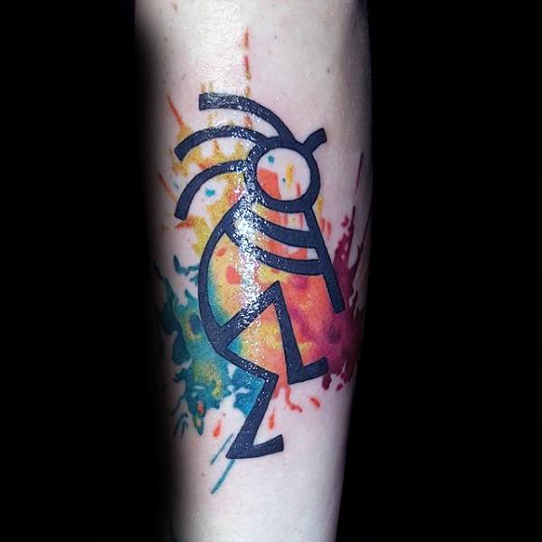 Black outlined Kokopelli tattoo with vibrant watercolor splashes in blue, green, yellow, and red bursting behind the figure.