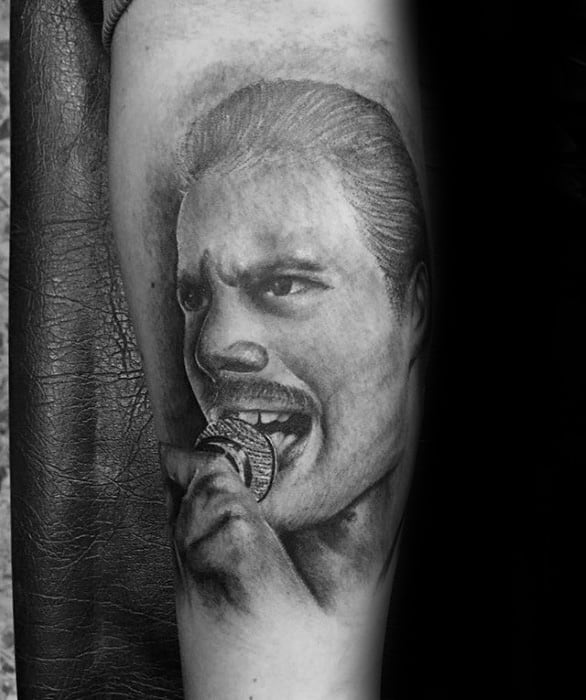 Black and grey tattoo of Freddie Mercury mid-performance, gripping a microphone with expressive eyes and detailed facial shading.